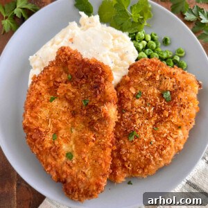 A perfectly fried Polish breaded pork chop (Kotlet Schabowy) served with creamy mashed potatoes and vibrant green peas on a plate.