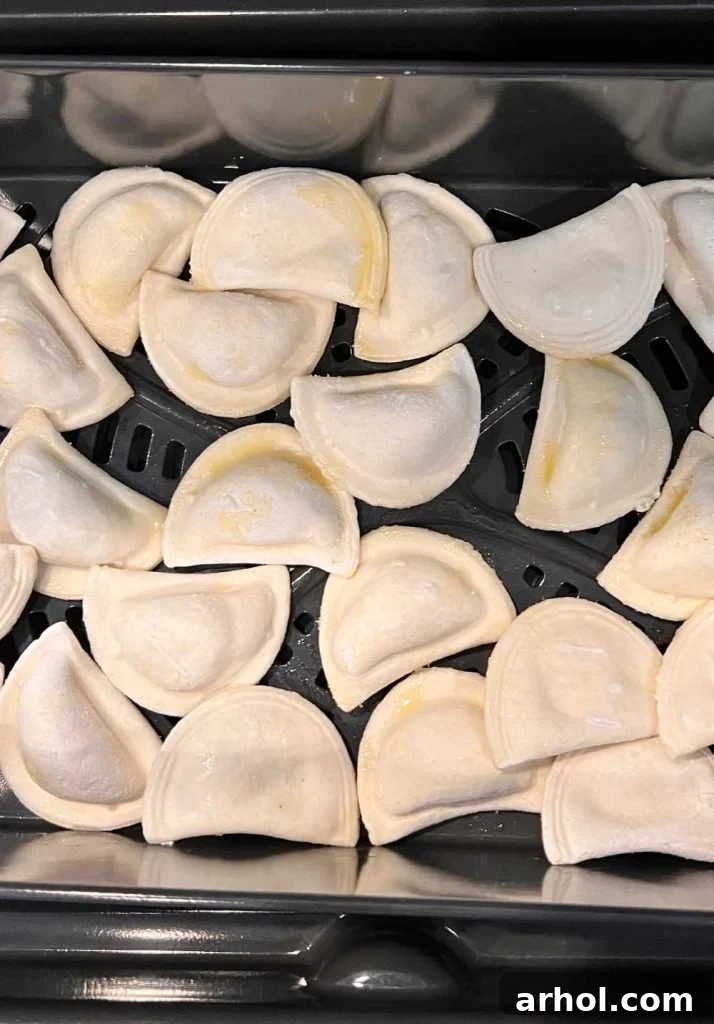 mini frozen pierogies in air fryer tray with olive oil spray