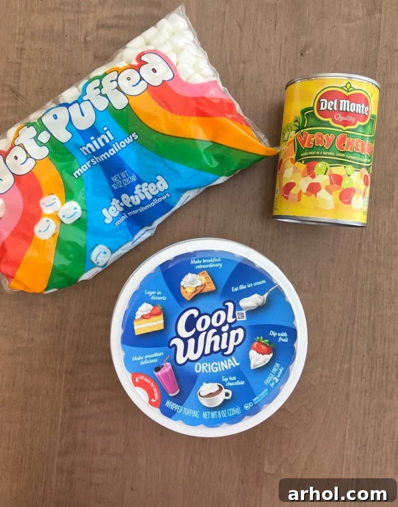 The three core ingredients for the fruit salad: a container of Cool Whip, a bag of mini marshmallows, and a can of mixed fruit cocktail, neatly arranged on a kitchen counter.