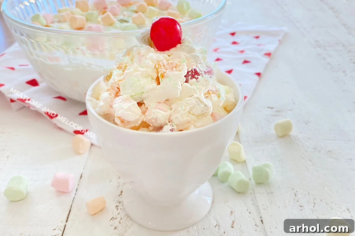 A close-up shot of Marshmallow Fruit Salad served in a sundae dish, with a bright maraschino cherry on top, highlighting its creamy texture and colorful fruit pieces.