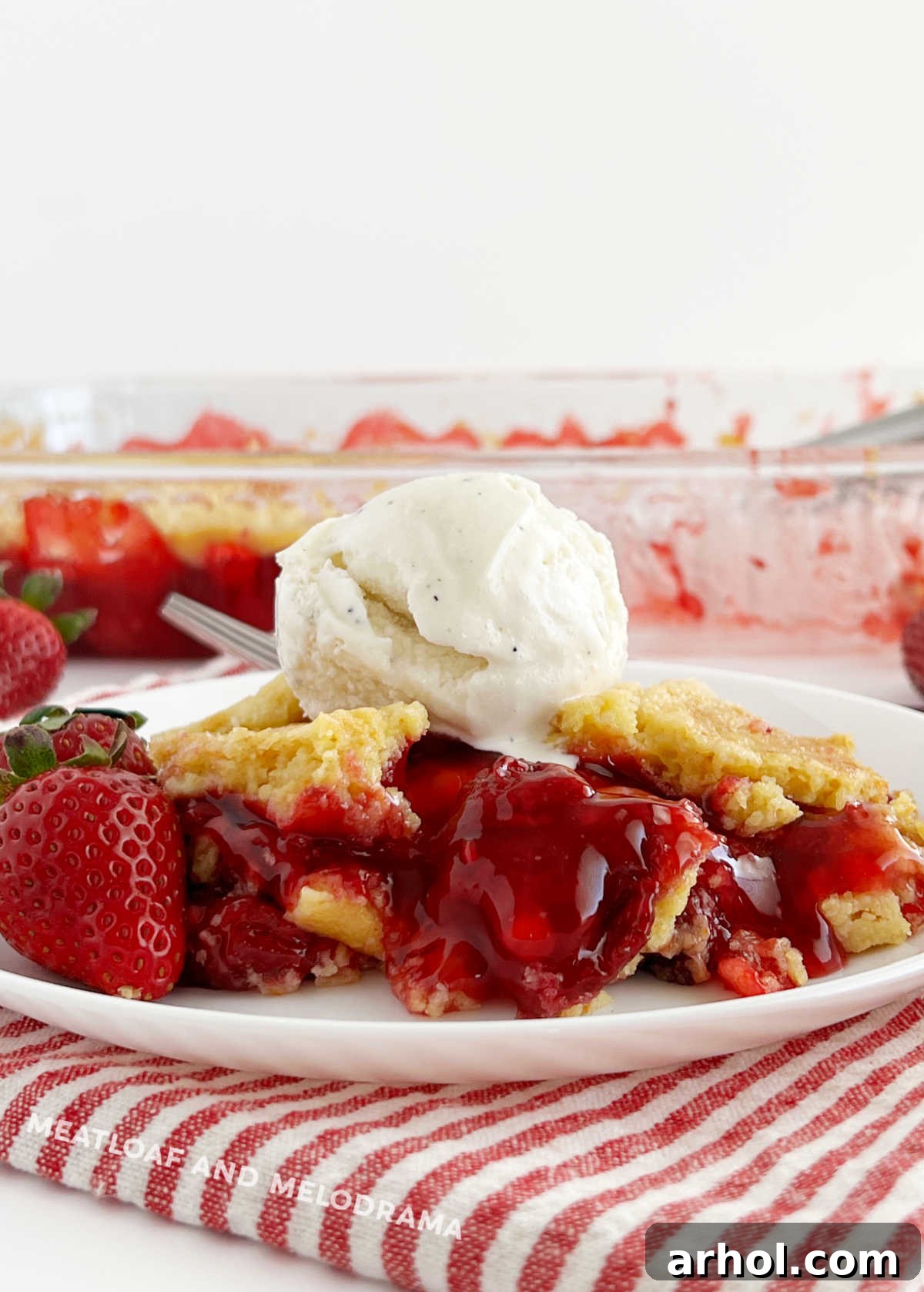 A slice of strawberry dump cake on a plate with fresh strawberries and a scoop of vanilla ice cream, showcasing its golden crust and fruity filling.
