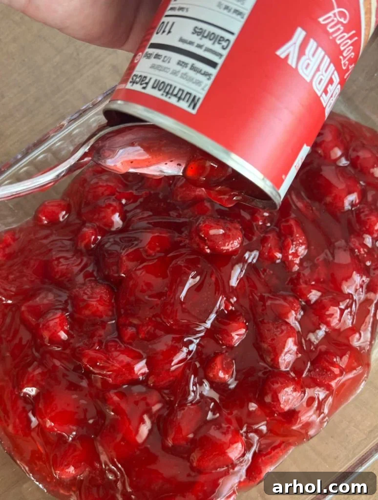 Spoonfuls of vibrant red strawberry pie filling being spread evenly into a baking pan.
