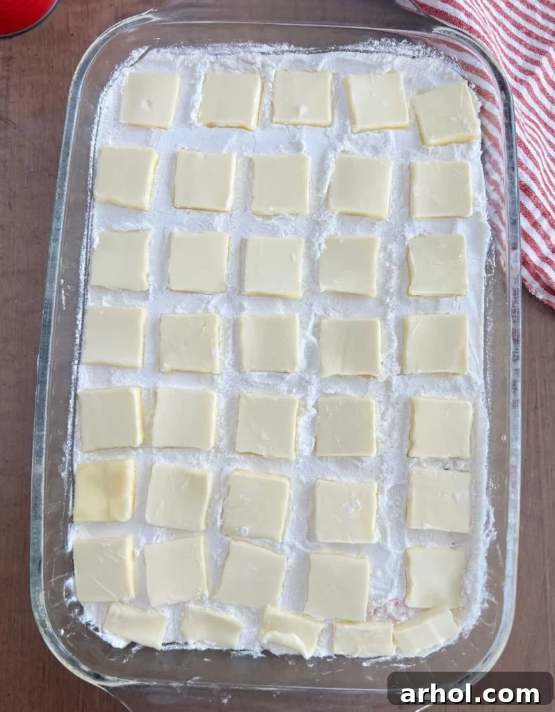 Thin slices of butter meticulously arranged in rows over the dry cake mix in a baking pan, ready for baking.