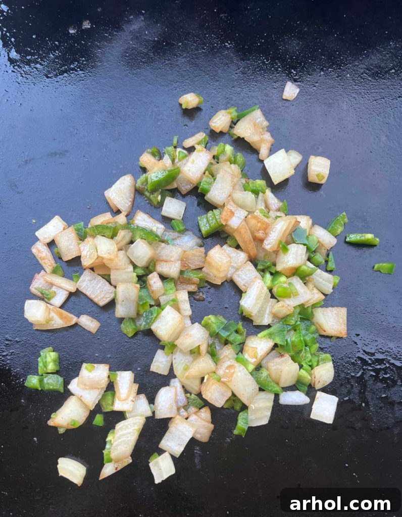 Diced onions and jalapeño peppers sizzling on a Blackstone griddle, cooking until softened.