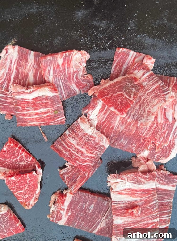 Thinly sliced ribeye steak searing on a hot Blackstone griddle, ready to be cooked and chopped.