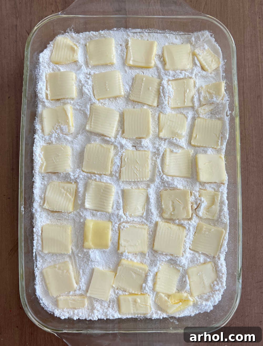 Butter Slices on Cake Mix Thin pats of butter carefully arranged in rows on top of the dry cake mix in the baking dish.