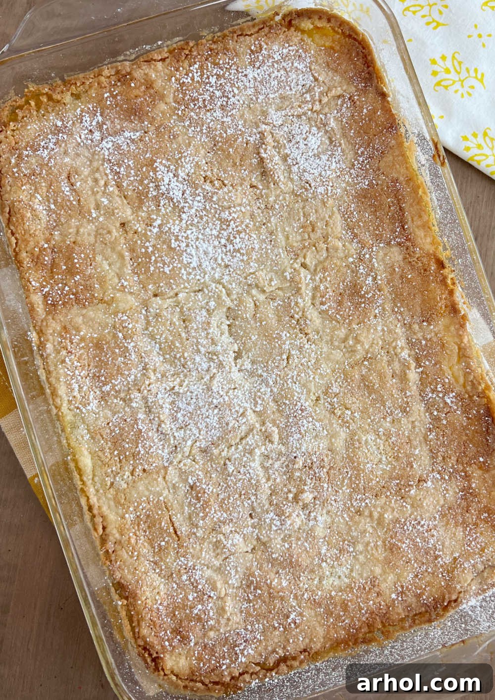 Baked Lemon Dump Cake Freshly baked lemon dump cake dusted with powdered sugar, resting on a wooden table.