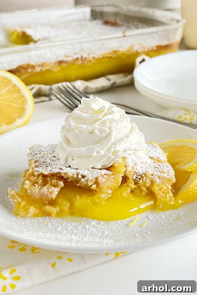Lemon Dump Cake Ready to Serve A beautiful slice of lemon dump cake adorned with powdered sugar and a dollop of whipped cream, presented on a white plate with a fork.