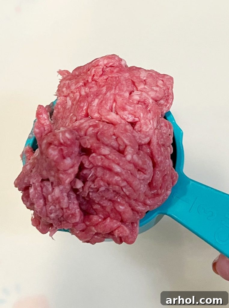 raw ground beef in a 1/3 measuring cup, ready to be formed into a loose ball.