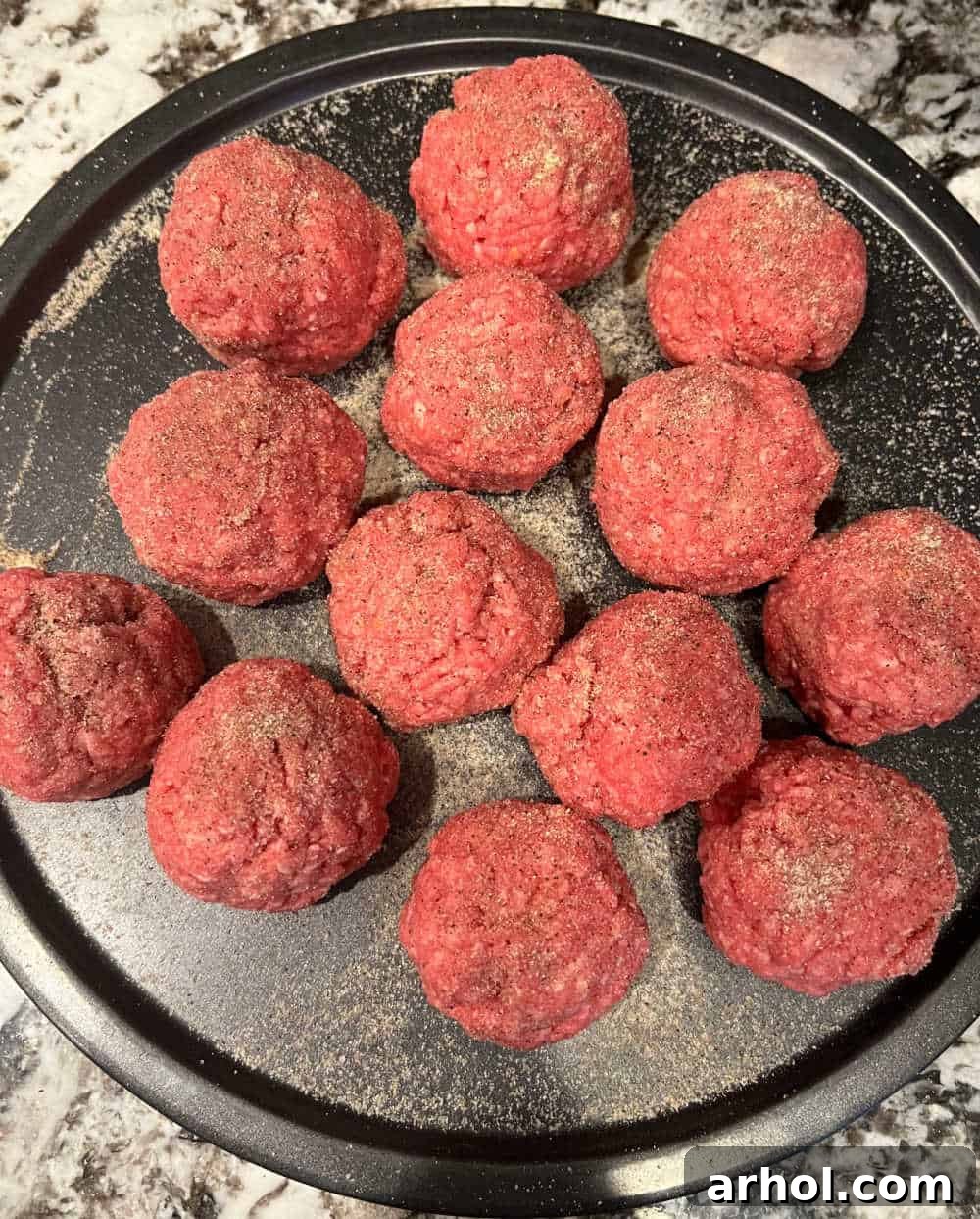 ground beef burger balls seasoned and ready on a tray, next to a hot griddle.