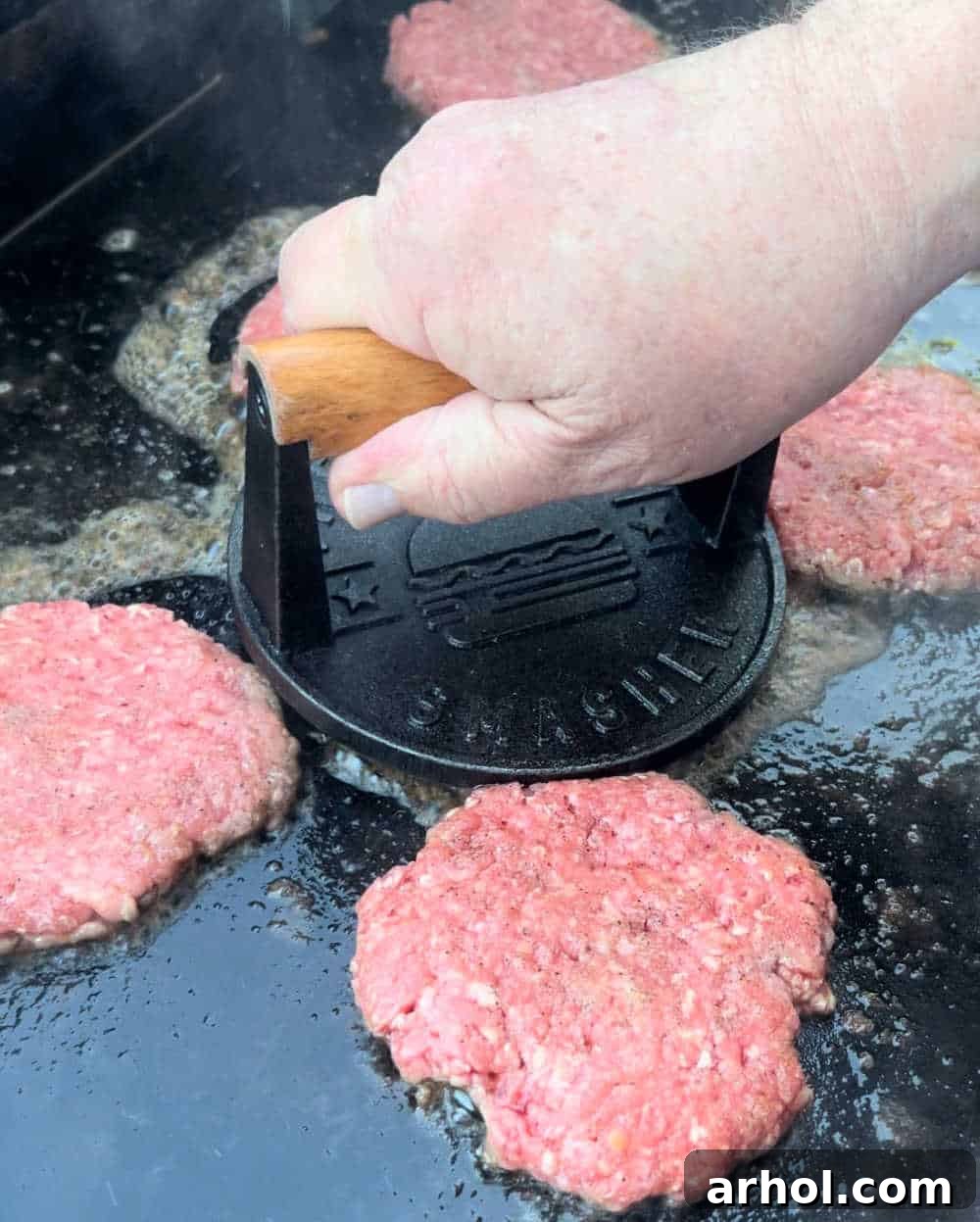 smash burger balls on a hot griddle with a burger press and parchment paper, being pressed into thin patties.