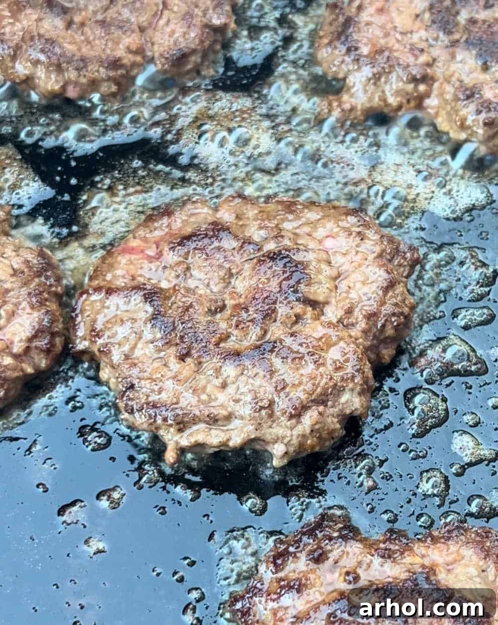 burgers cooking on a blackstone griddle, with one side perfectly crispy and golden-brown.