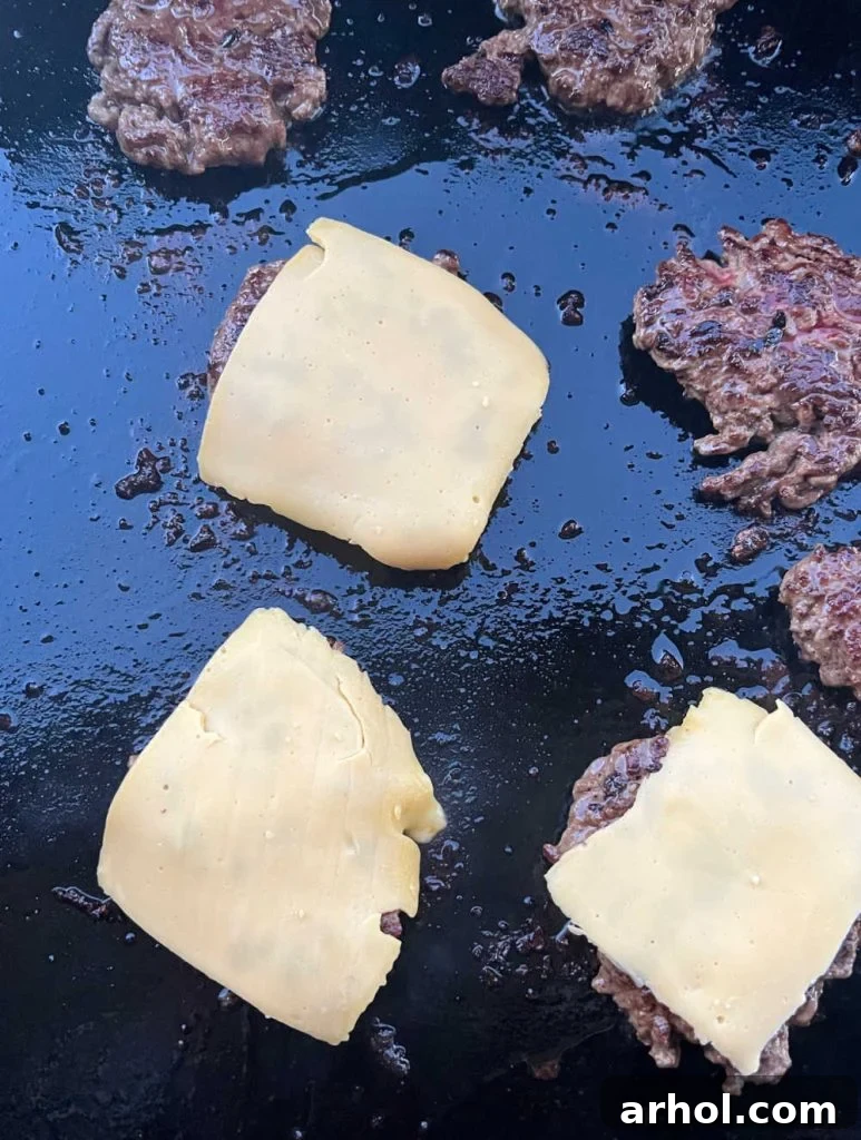 burger patties on a blackstone griddle with American cheese slices melting on top.