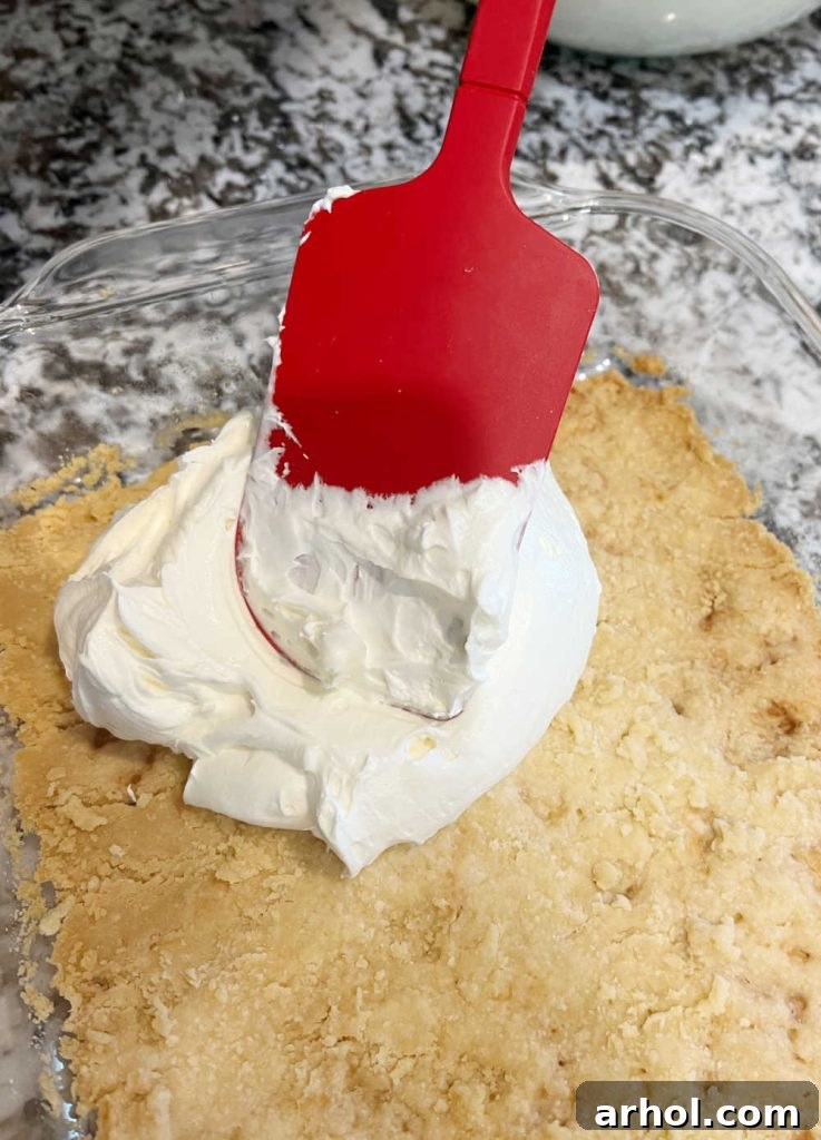 Spreading the smooth cream cheese mixture over the cooled shortbread crust in the baking pan.