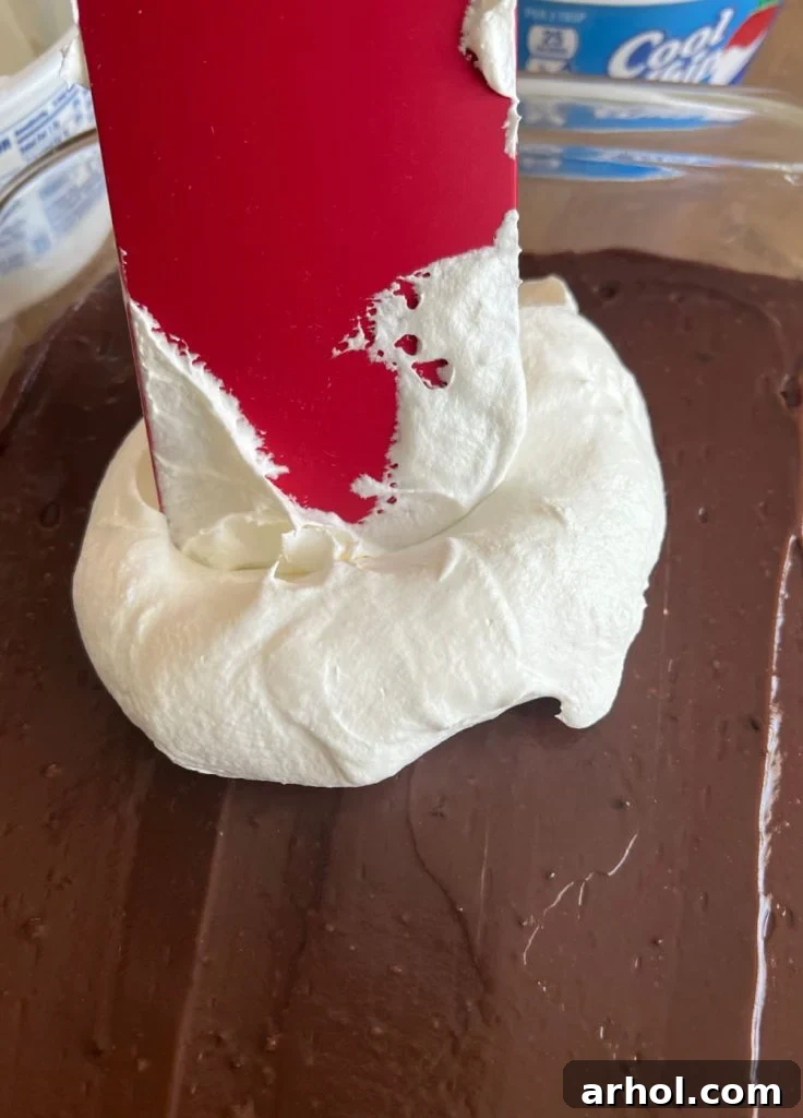 Spreading a generous layer of Cool Whip over the set chocolate pudding in the baking dish.