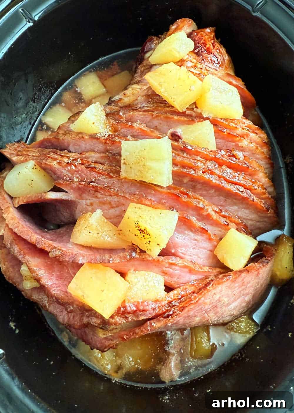A perfectly cooked spiral cut ham in a slow cooker, glistening with pineapple and brown sugar glaze.