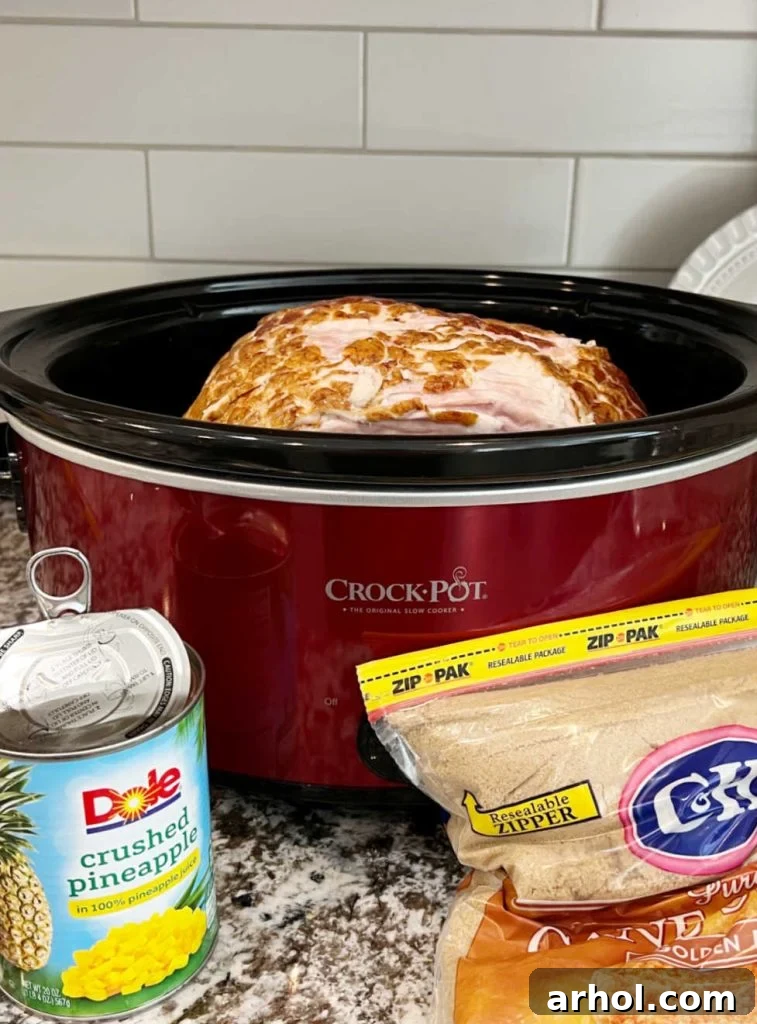 Crushed pineapple and brown sugar layered over a spiral ham in a crock pot, ready for cooking.