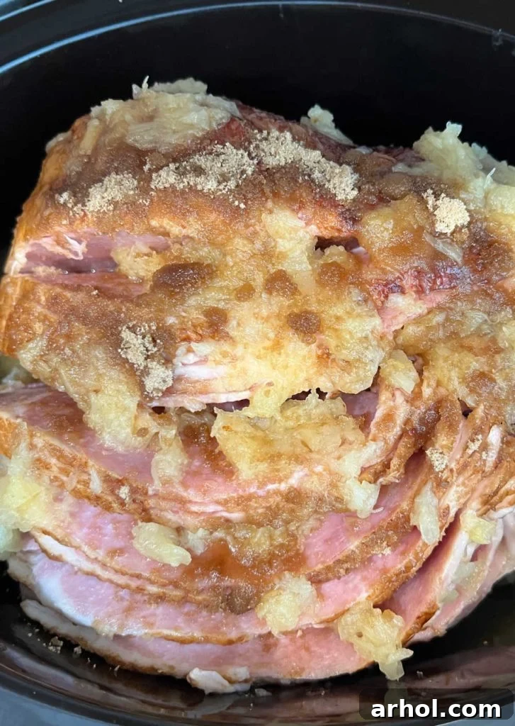 A spiral ham nestled in the slow cooker, ready to cook, topped with brown sugar and pineapple.