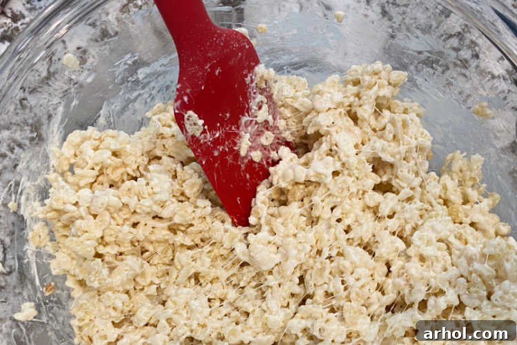 Mixing crisp rice cereal into the melted marshmallow mixture until fully coated.