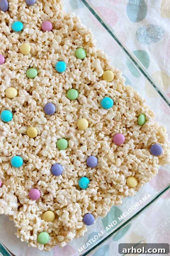 Pan of bright spring rice krispies treats topped with an array of pastel M&M candies, ready to be cut.