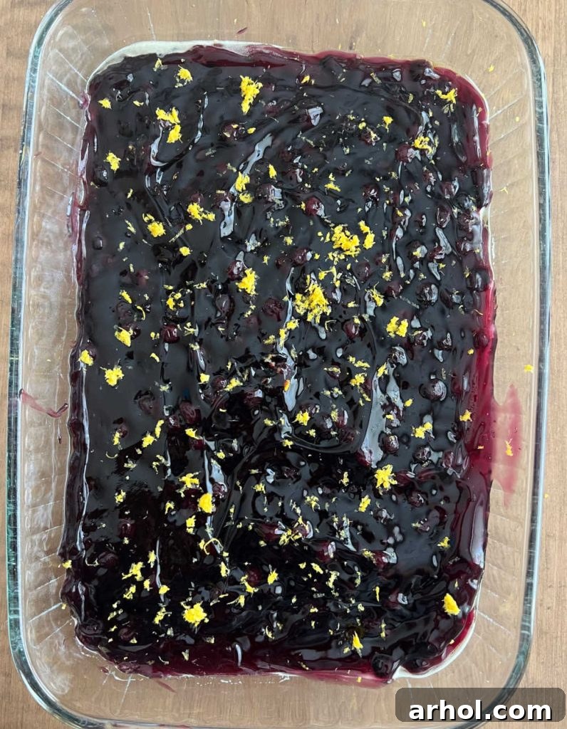 Two cans of blueberry pie filling and fresh lemon zest spread evenly in a 9x13 inch baking pan.