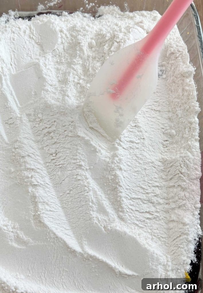 Vanilla cake mix being gently spread over the blueberry pie filling layer in a baking pan using a spatula.