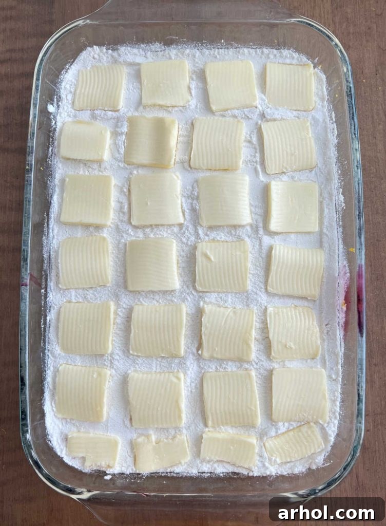 Thin slices of butter arranged neatly in rows over the dry cake mix in a baking pan, ready for the oven.