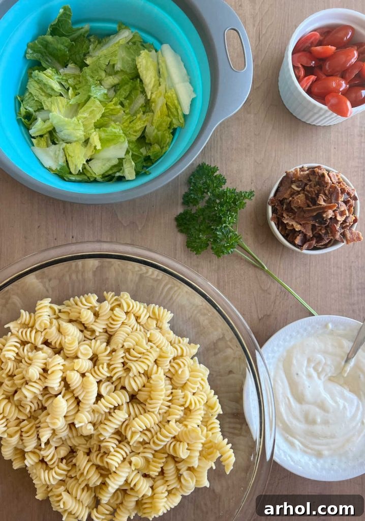 Perfect BLT Pasta Salad 3 Assorted ingredients for BLT pasta salad: rotini pasta, fresh romaine lettuce, juicy tomatoes, crispy bacon, and creamy dressing, neatly arranged on a rustic wooden table.