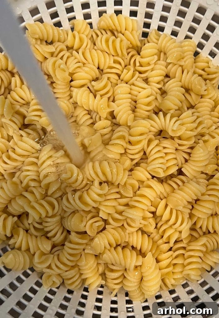 Perfect BLT Pasta Salad 4 Cooked rotini pasta being rinsed under cold water in a colander, a crucial step for a perfect cold pasta salad.