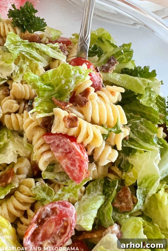 Perfect BLT Pasta Salad 6 Scoop of BLT pasta salad with rotini, fresh lettuce, and sliced tomatoes on a serving spoon, garnished with extra bacon bits.