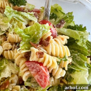 blt pasta salad with rotini pasta and bacon and lettuce and tomatoes on a spoon, showcasing its creamy texture