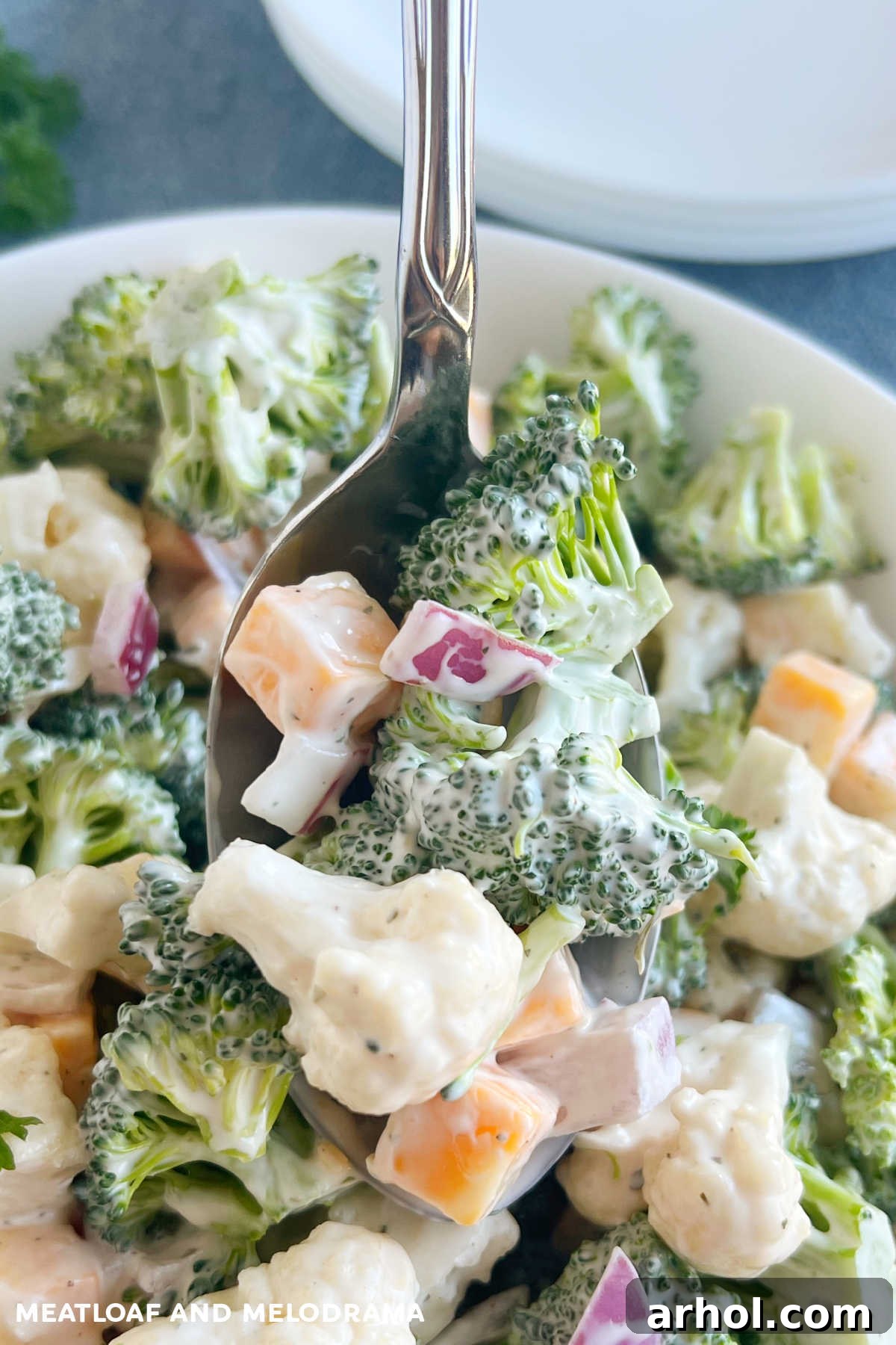 Vibrant broccoli and cauliflower salad with cheese cubes and red onions, coated in a rich, creamy mayonnaise-based dressing, presented on a serving spoon