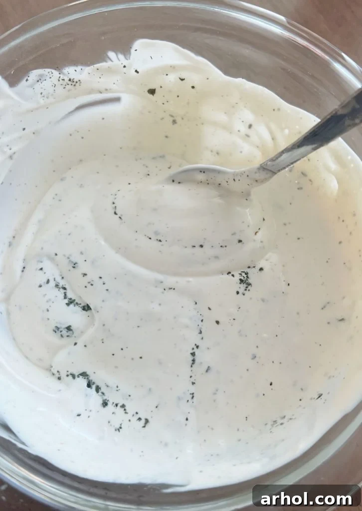 Close-up of a small mixing bowl where mayonnaise, sour cream, and red wine vinegar are being whisked together to form the creamy dressing