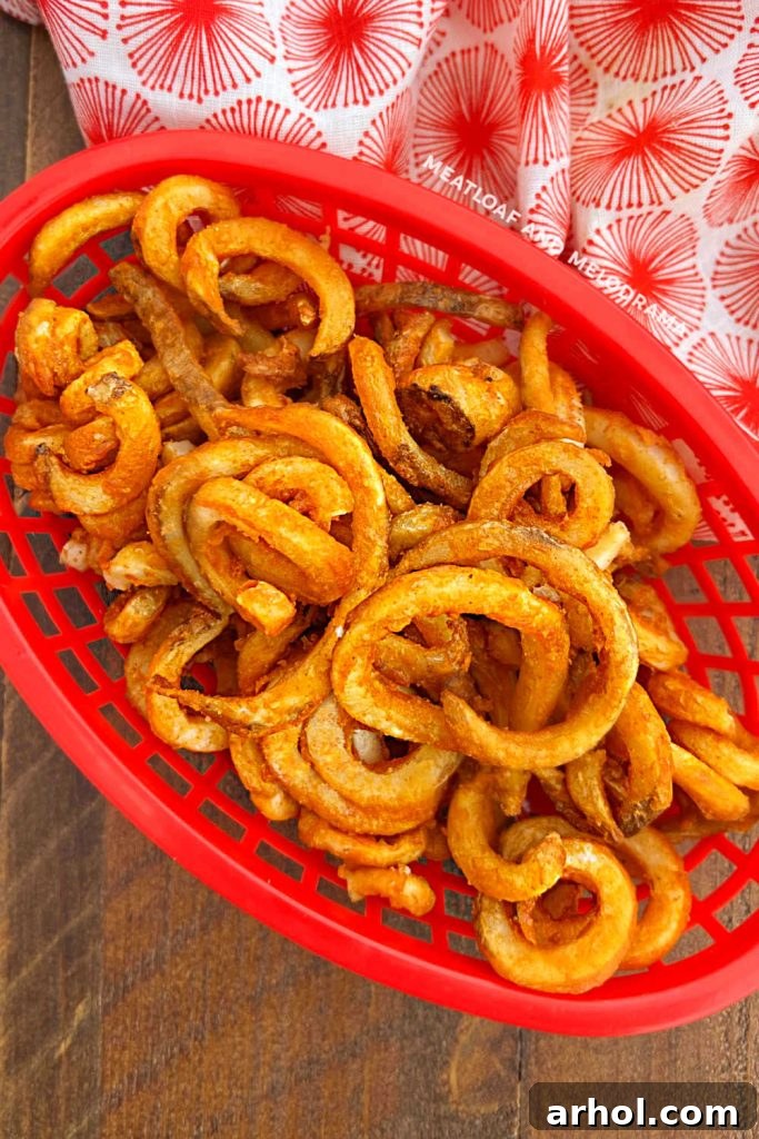 Freshly air-fried Arby's curly fries in a red serving basket on a table, ready to be enjoyed.