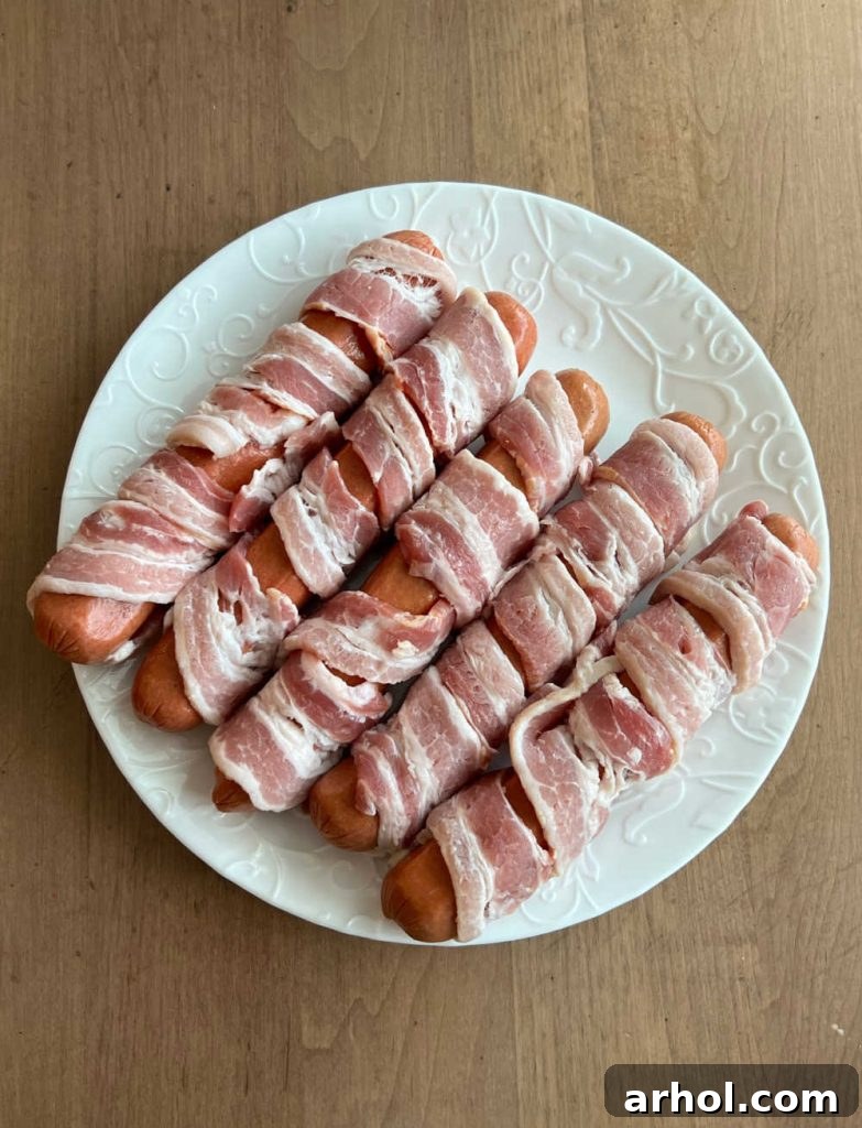 Authentic Sonoran Hot Dogs Blackstone Griddle Style 4 Raw hot dogs meticulously wrapped in bacon strips, ready for cooking.
