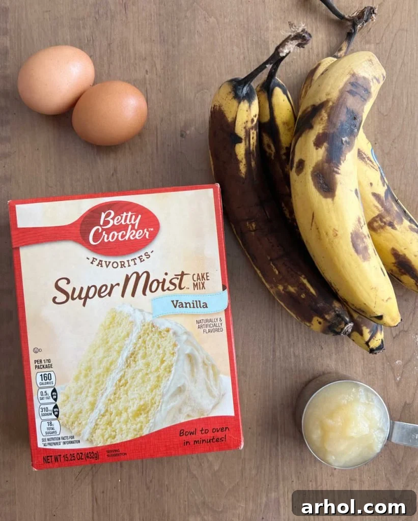 The four simple ingredients for cake mix banana bread: a box of cake mix, eggs, ripe bananas, and applesauce laid out on a table.