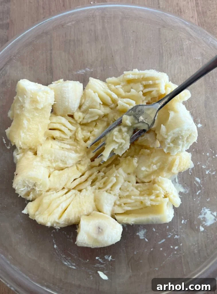 Close-up of ripe bananas being mashed in a mixing bowl with a fork, showing their soft texture.