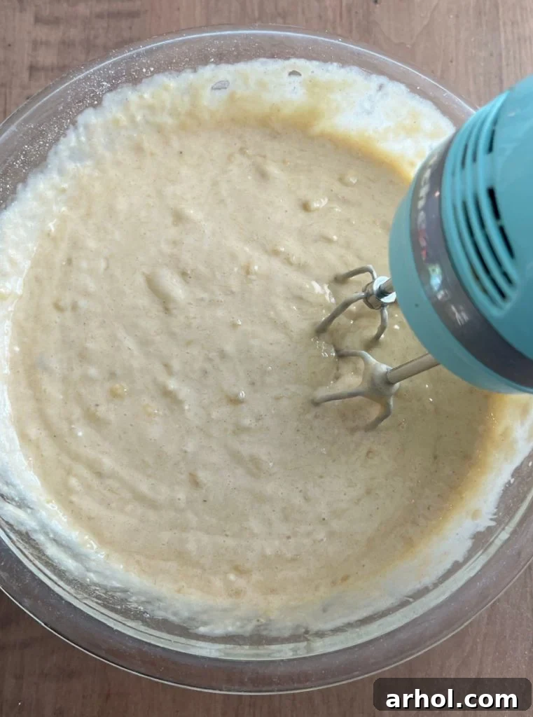 Banana bread batter being mixed with a hand mixer in a large bowl, showing its combined texture.