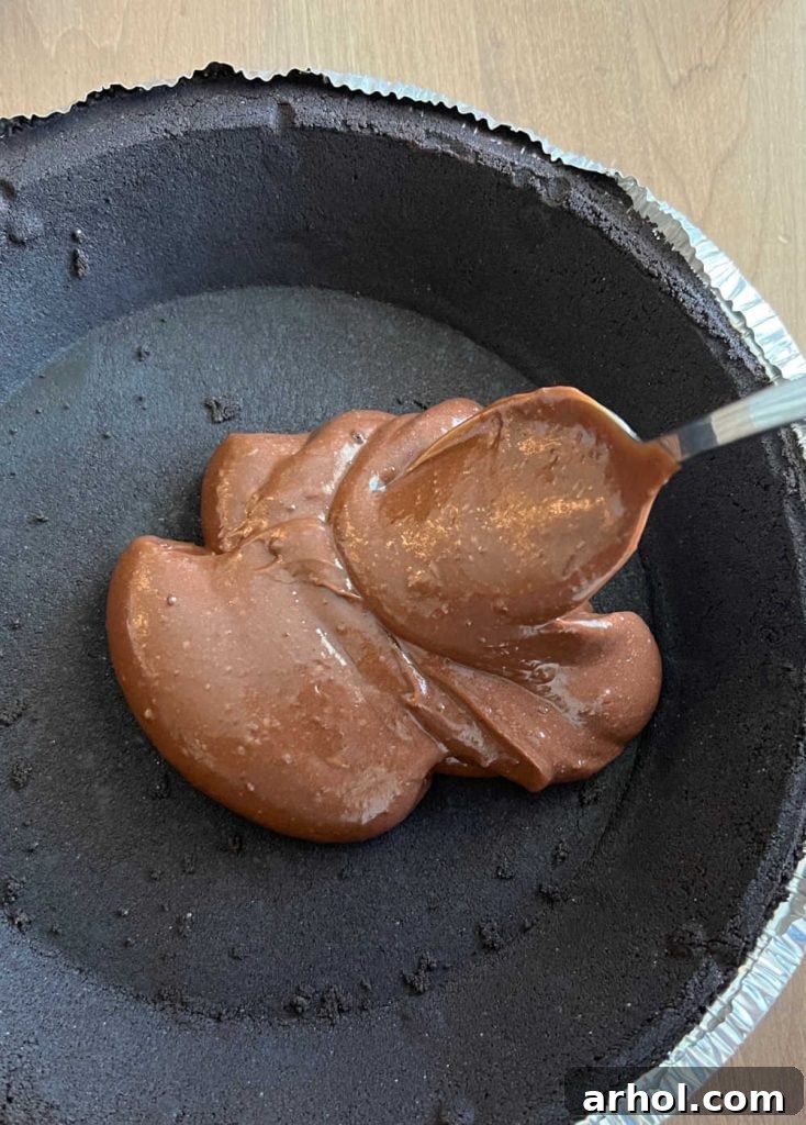 Spoon instant chocolate pudding into the bottom of an Oreo cookie pie crust, spreading it evenly for the first layer of the no bake pie
