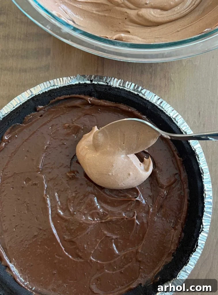Spoon the cool whip and chocolate pudding mixture over the dark chocolate pudding layer in the pie crust, creating a second distinct layer