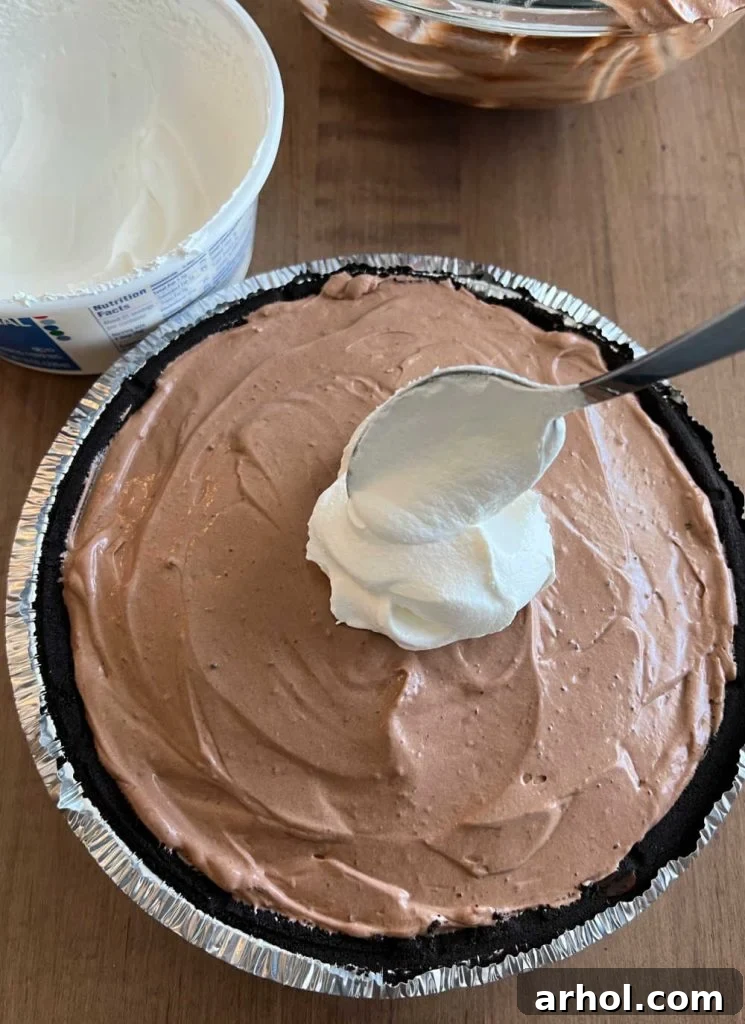 Spoon and spread the remaining Cool Whip whipped topping evenly over the chocolate pudding layers in the pie crust