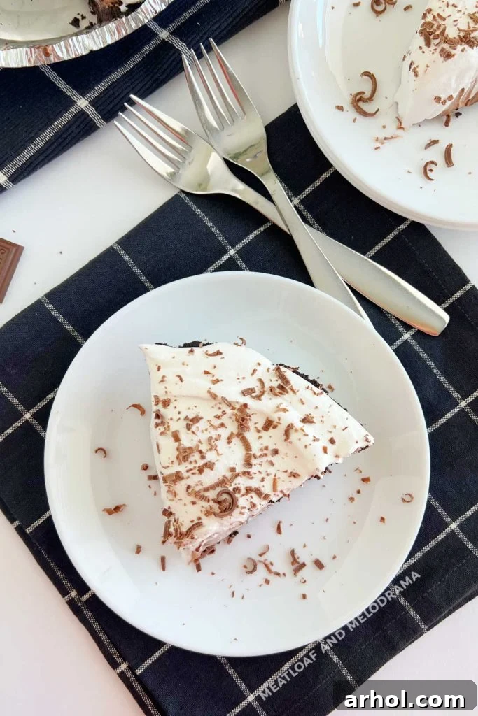 A perfectly cut slice of No Bake Chocolate Pudding Pie showing distinct layers of chocolate pudding, mixed pudding with whipped topping, and pure whipped topping, garnished with chocolate shavings, on a white plate