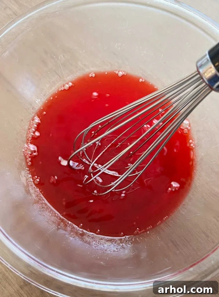 Whisking strawberry Jello powder and hot water in a mixing bowl until fully dissolved.