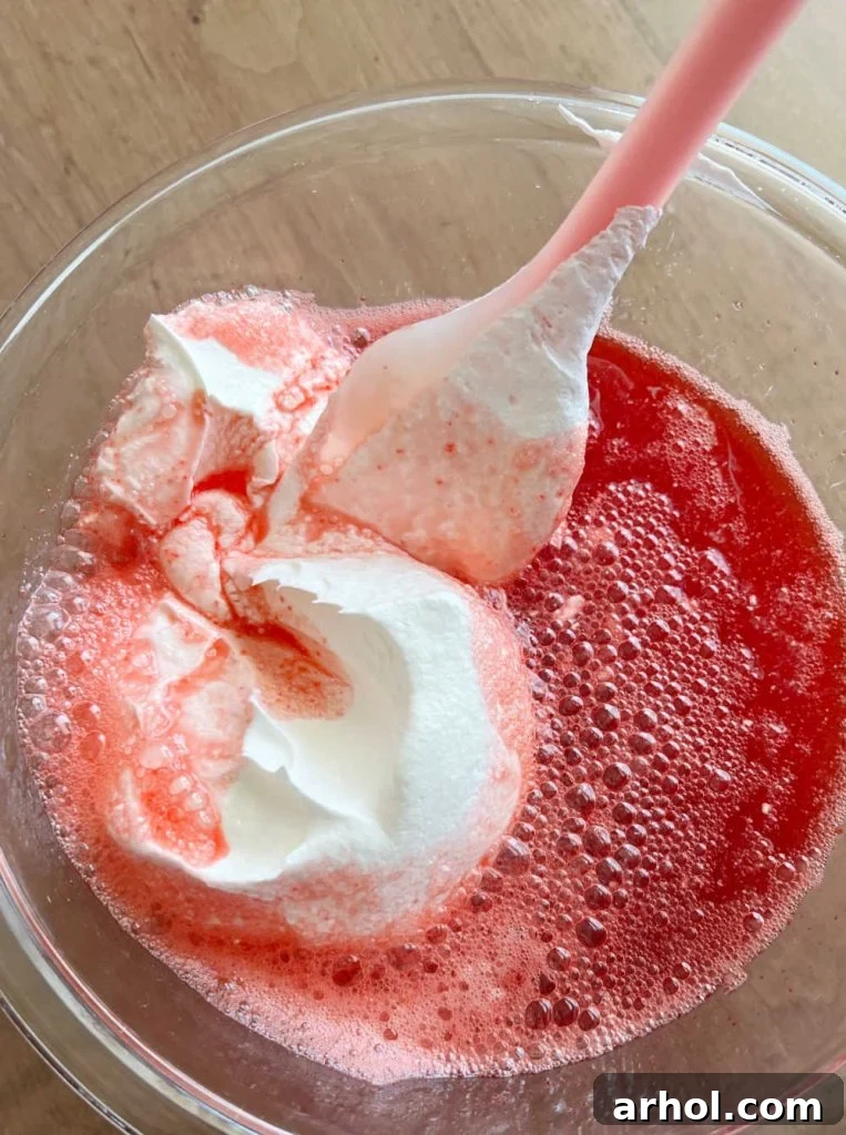 Gently stirring thawed Cool Whip into the pink Jello mixture to create a creamy pie filling.