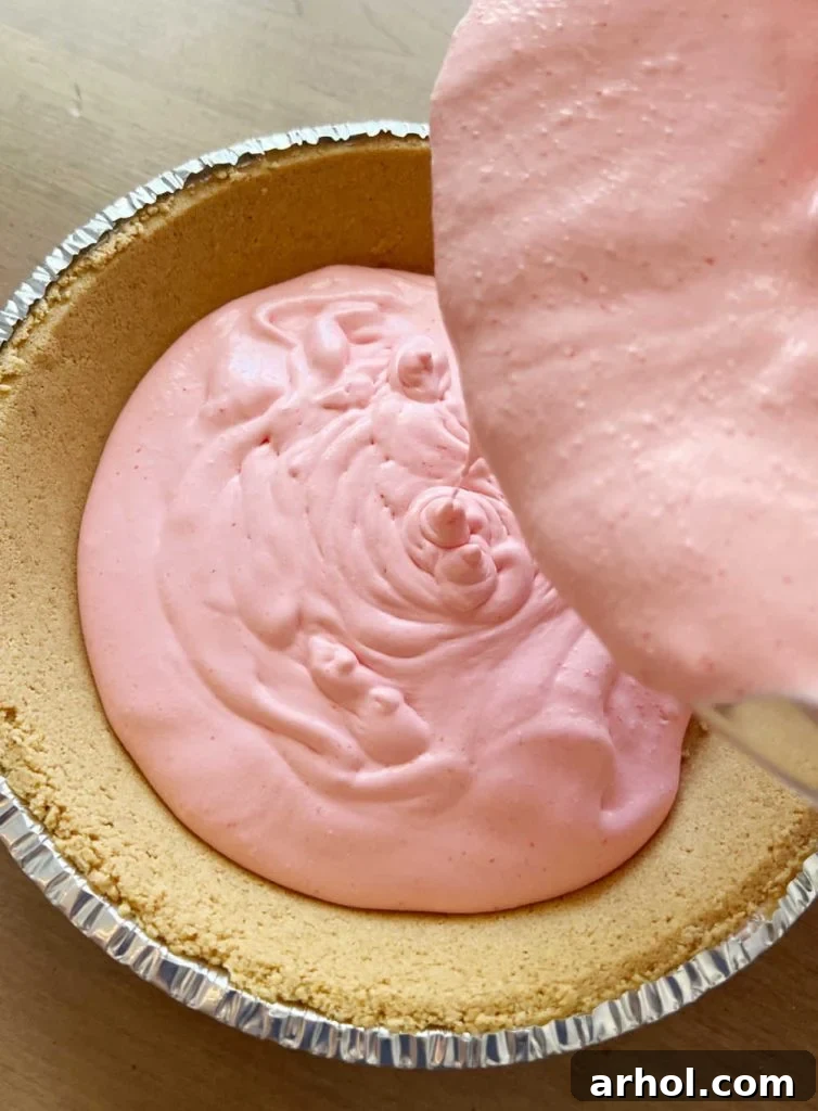 Spoon the thick strawberry Jello and Cool Whip mixture into a graham cracker pie shell, ready for chilling.