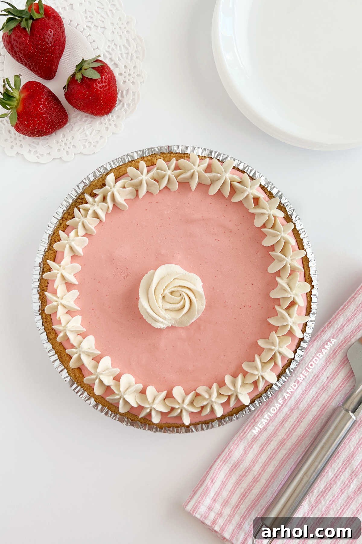 A beautifully set No Bake Strawberry Cool Whip Pie, garnished with fresh strawberries and whipped cream rosettes, sitting on a table.