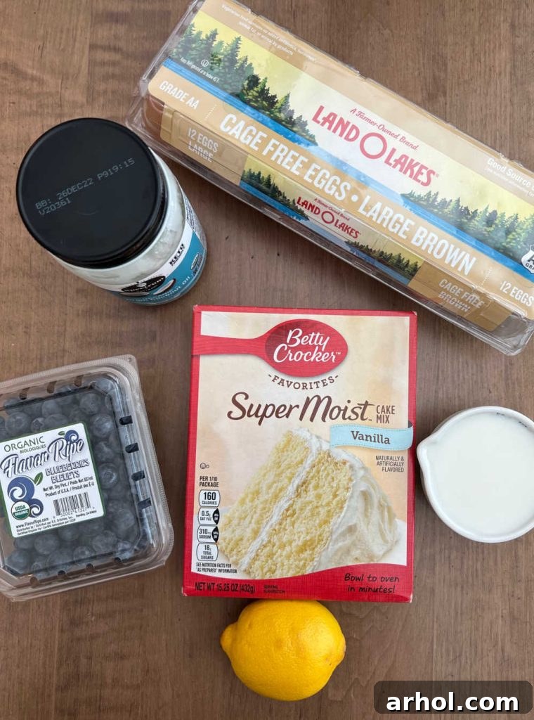 Simple Ingredients for Quick Blueberry Muffins Essential ingredients for cake mix blueberry muffins arranged on a clean kitchen surface: a box of vanilla cake mix, fresh blueberries, coconut oil, eggs, milk, and a fresh lemon