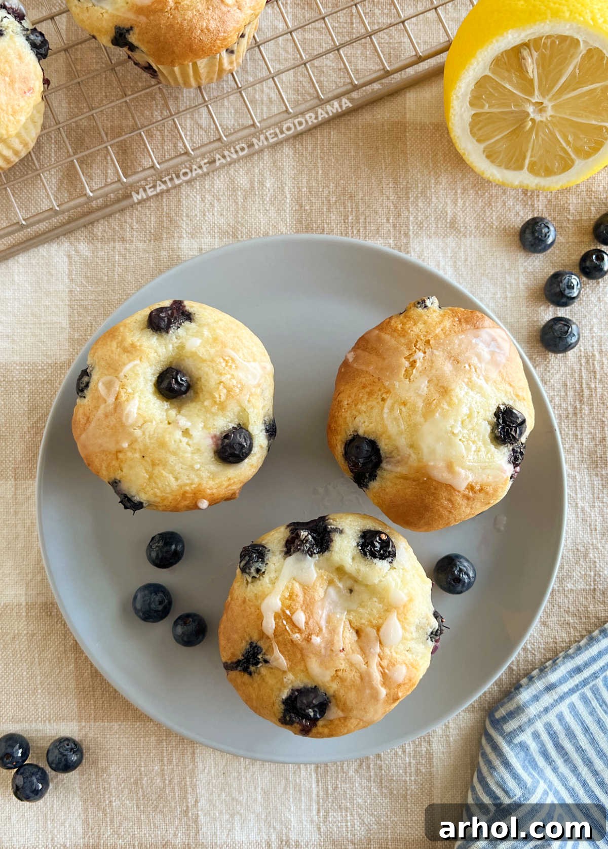 Lemon Glazed Cake Mix Blueberry Muffins Ready to Serve A plate featuring several moist cake mix blueberry muffins, each artfully drizzled with a sweet and tangy lemon glaze and garnished with lemon zest