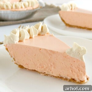 A perfectly portioned slice of Jello orange creamsicle pie, artfully topped with a swirl of whipped cream, presented on a white plate, highlighting its smooth texture and inviting color.