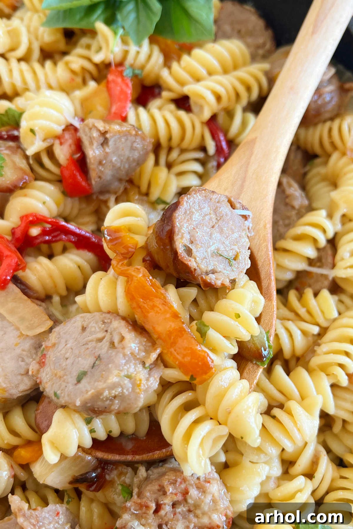 Italian sausage and peppers pasta on a wooden spoon, showcasing a colorful and delicious meal